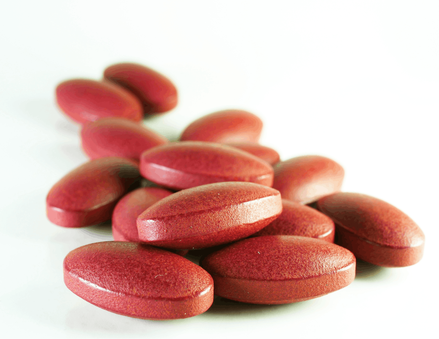 A pile of red ferrous sulphate iron tablets, representing the most commonly prescribed but poorly tolerated form of iron supplementation