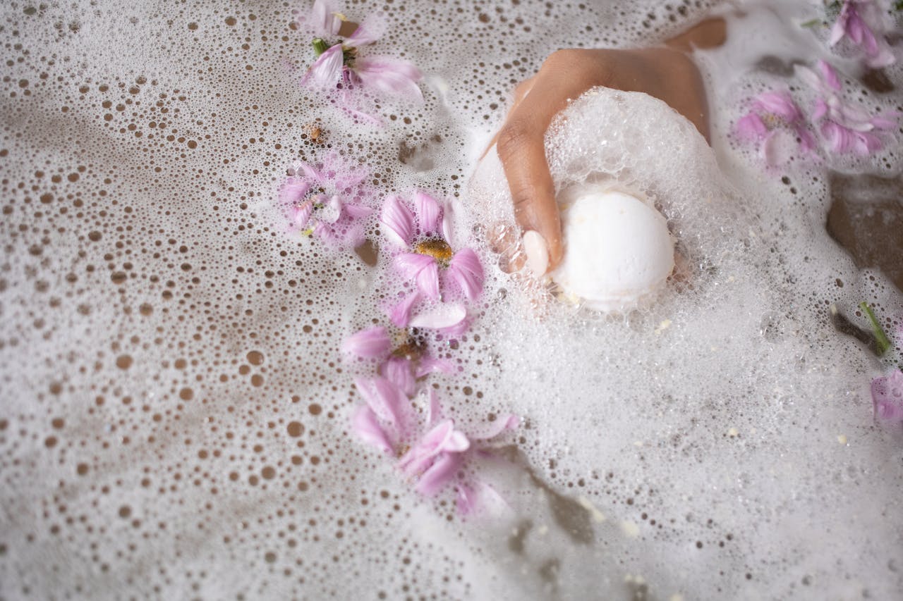 Baby hand in a bubble bath with pink flowers – safe baby skincare and bath product awareness