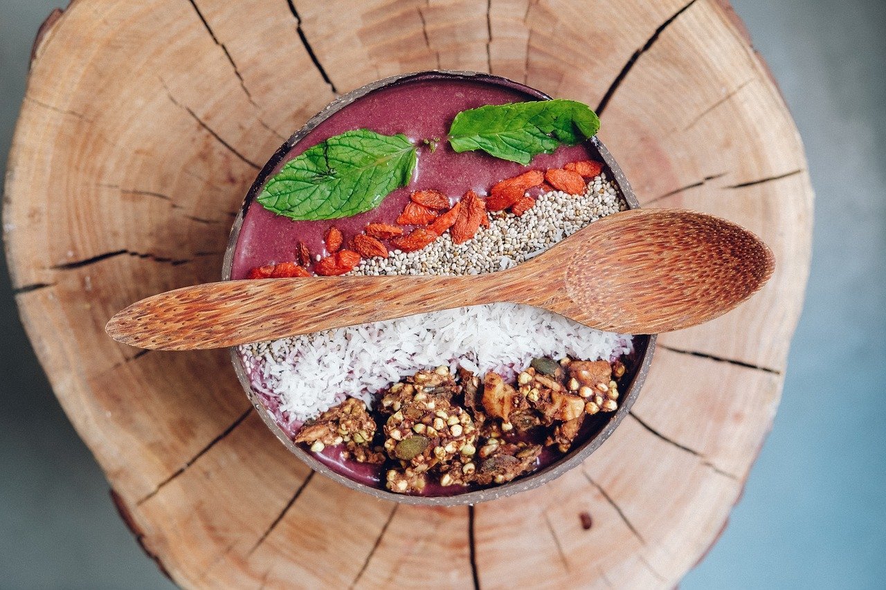 Healthy acai bowl topped with granola, coconut flakes, and mint leaves on a wooden background