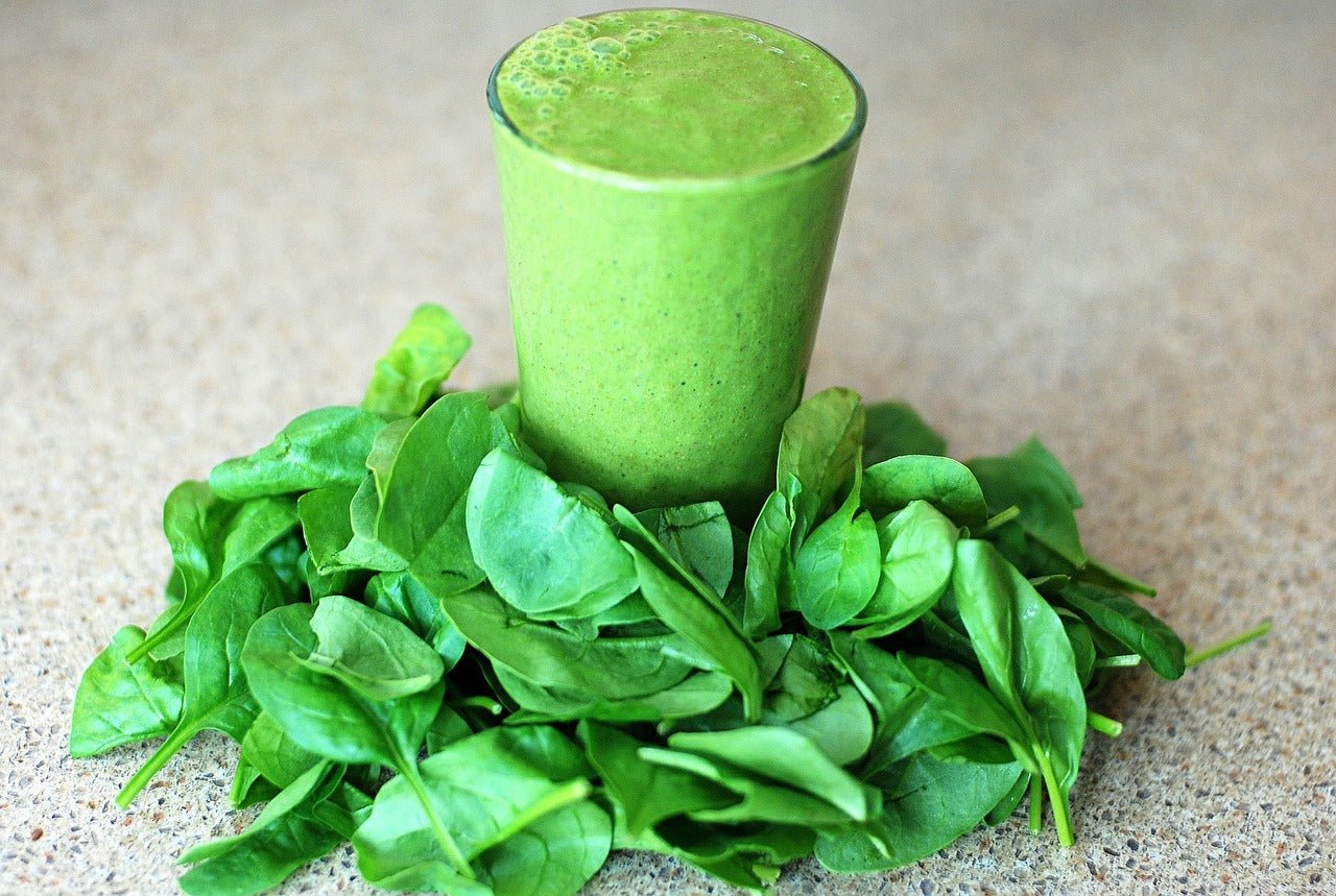Green apple, spinach and mint smoothie in a glass surrounded by fresh spinach leaves