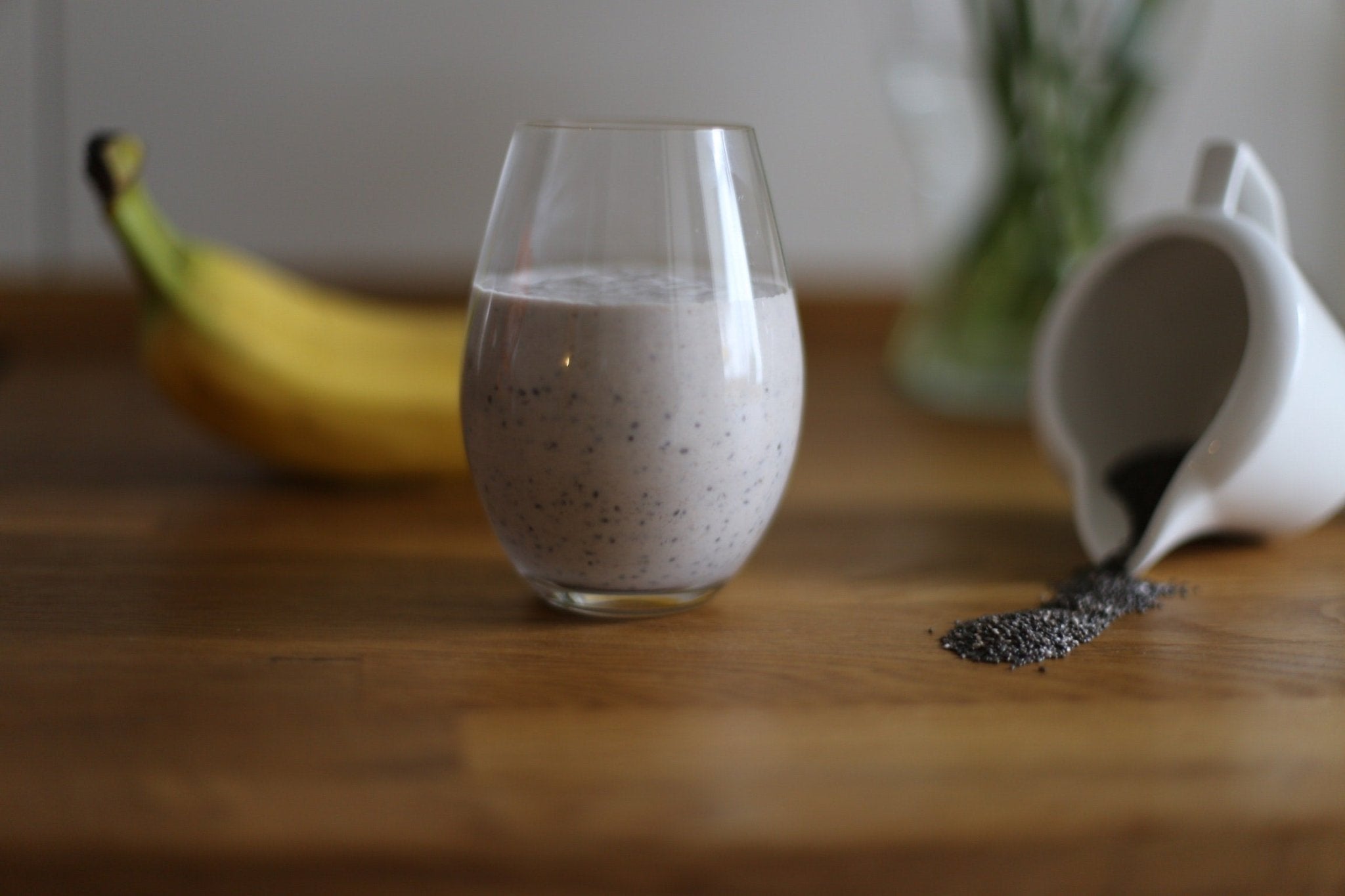 Peanut butter banana smoothie in a glass with banana and chia seeds on a wooden table