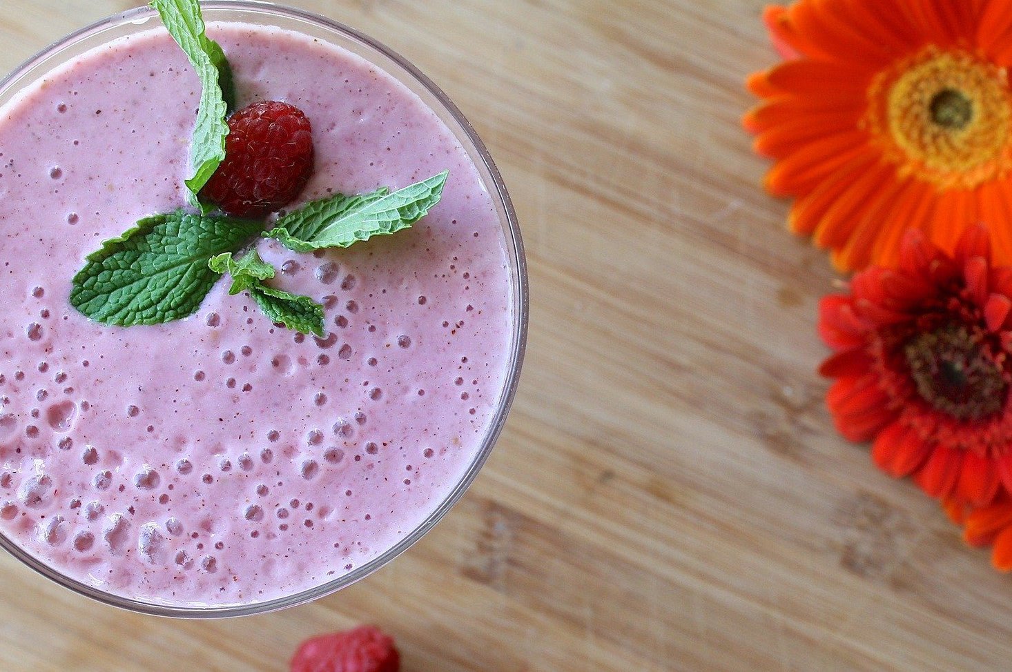 Blueberry banana smoothie with mint garnish in a glass, served on a wooden board with fresh flowers