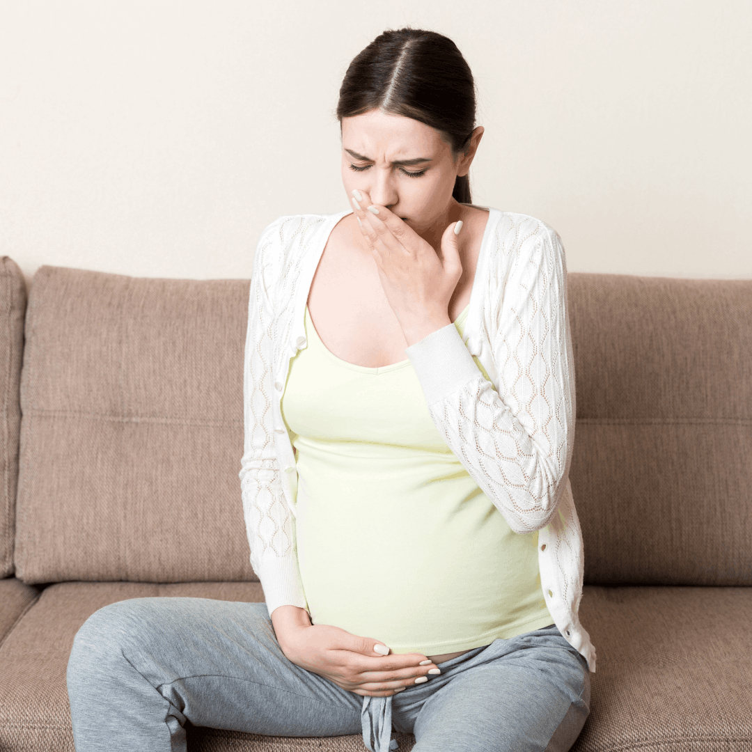 Pregnant woman sitting on couch experiencing morning sickness nausea in first trimester