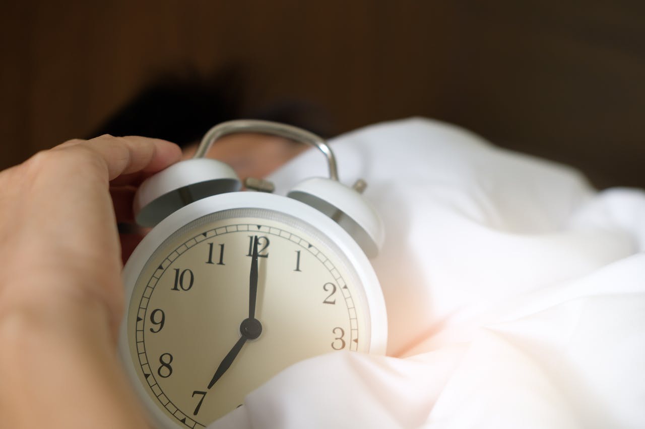 Hand holding alarm clock in bed – Myo-Inositol and sleep quality connection