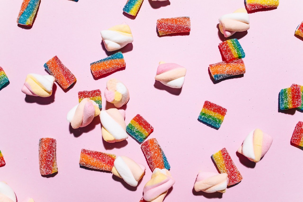 Colourful lollies scattered on a pink background, representing foods high in sugar that can cause blood sugar spikes